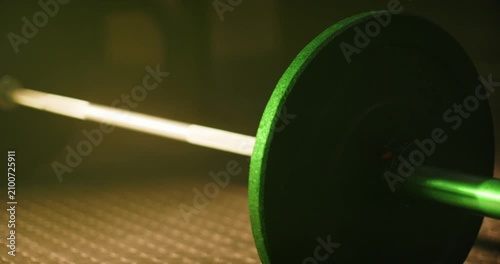 Camera is shifting, light is brightening, green plate and bar are revealing rubber floor at gym