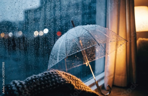 Transparent umbrella resting by window on a rainy day with bokeh lights