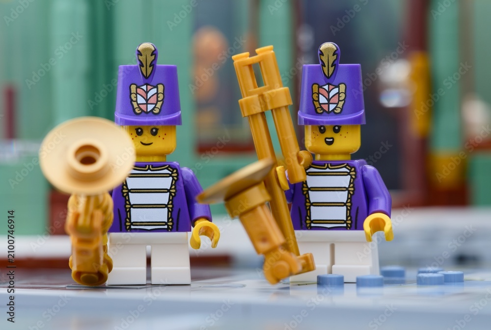 Fototapeta premium Tambov, Russian Federation - July 14, 2026 Two Lego marching band musician minifigures wearing purple uniforms and tall hats hold golden wind instruments on a city street.