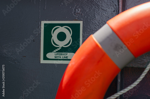 Lifebuoy mounted on board an offshore support vessel adjacent to its identification sign. The life-saving appliance is positioned for immediate deployment during a man overboard emergency.