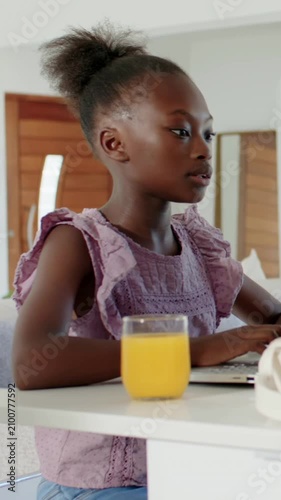 Vertical video: Typing student in purple top studying at kitchen table with laptop and orange juice