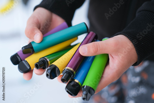 A child is holding many colorful vapes. A dangerous addiction. Vaping among teenagers.