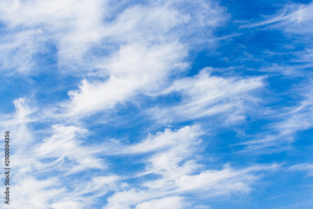 Fototapeta premium Streaks of white clouds trail across a clear blue sky.
