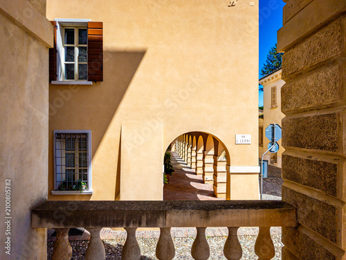 Sabbioneta, Italy, old building facade showing an archway with a repeating pattern of arches, windows, a stone balustrade, and long shadows creating geometric shapes on the wall