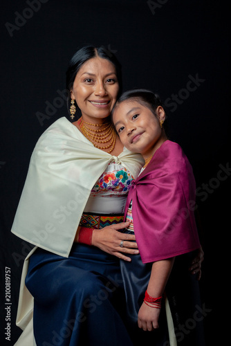 Indigenous Kichwa mother and daughter from Otavalo, Ecuador, wearing traditional hand-embroidered blouses and anaco sharing affectionate moments of cultural heritage in a studio portrait