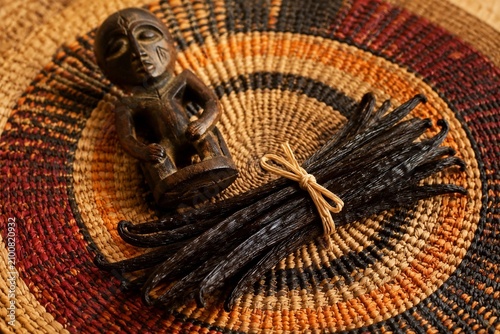 A handwoven raffia table mat with vanilla pods and a wooden carving.