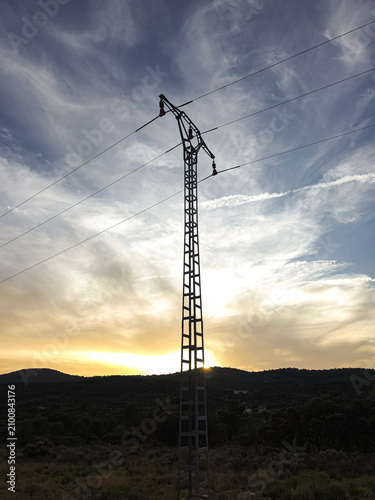 Fotografía High voltage power line pylon stands against sunset sky over rural mountains