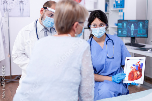 Cuadro en lienzo Senior woman discusses arrhythmia symptoms with a cardiologist during a masked hospital examination focused on diagnosis and care