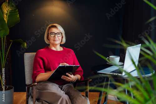 Portrait of 50's stylish, confident mature businesswoman, middle aged experienced senior female professional, business coach, mentor, therapist, counselor working on laptop in office. Female leader