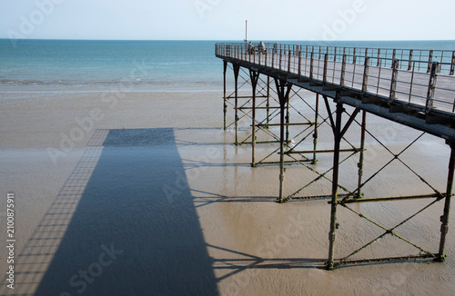Bognor Regis  West Sussex England UK. 14.07.2026. A weathered pier extends over a wet sandy shore during low tide, with the ocean in the background under a clear sky