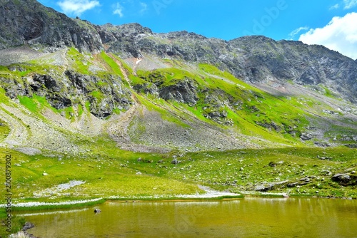 Obraz na plátne Mountain range with rock cliffs, scree and green alpine meadow above the shore o