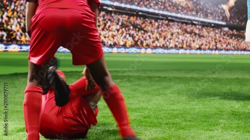 Red soccer player falling on ground in pain after dangerous tackle, teammates protesting and asking for foul sanction after injury, footballer rolling on grass, soccer drama during match.