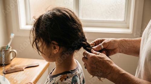 Elderly hands braiding little girl hair in bathroom