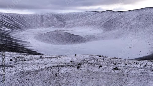 Aerial pull back of a hiker on massive snow covered volcanic crater in Northern Iceland - Horizontal pull away drone shot