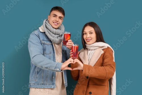 Happy couple with glasses of delicious mulled wine showing heart gesture on b...