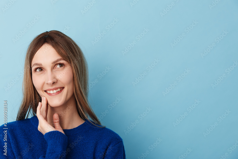 Obraz premium A fresh, friendly portrait of a smiling woman in a blue sweater inside a studio, posing closeup with a relaxed posture. Soft lighting highlights confidence and casual style in a bright, welcoming
