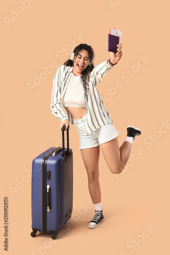 Young African-American woman with suitcase and passport with ticket listening...