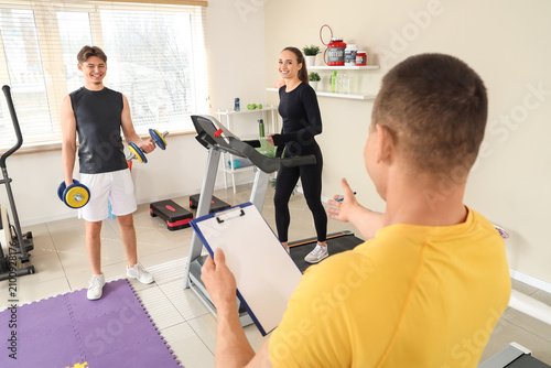 Male coach with clipboard and young people training in gym