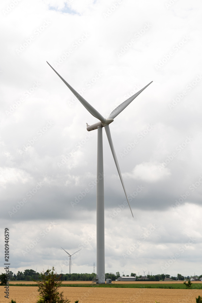 Fototapeta premium A modern wind turbine towers over rural land beneath a dramatic cloudy sky, symbolizing renewable energy, clean power, and sustainable electricity.