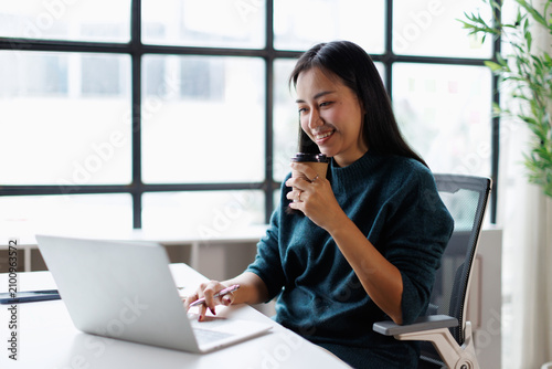 Foto Young asian woman smiling and working with a laptop at a modern office desk, dri
