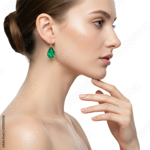 Young caucasian woman with a side profile, wearing a teardrop emerald earring, gently touching her chin in a studio setting, serene elegance and luxury atmosphere