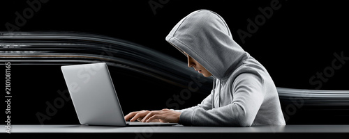 A hooded hacker figure working at a computer, with digital code flowing in the background, leaving room for copy space to the side.
