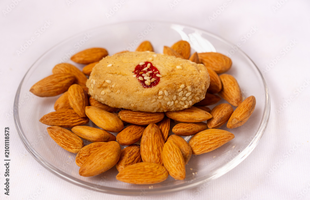 Fototapeta premium Side view of a single homemade sesame cookies in a included jam filled with almonds nuts on a glass plate, sweet cookies snacks, isolated on a white background.