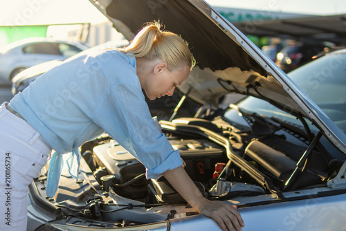 Fotografie Woman looking into the open hood of a broken-down car, experiencing mechanical i