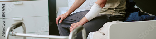 Konstfotografi Header of unrecognizable man sitting on hospital bed with bandaged arm in military medical ward, recovering from injury