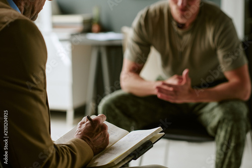 Bild auf Leinwand Young adult man in military hospital receiving counseling session, discussing recovery and mental health support with clinician