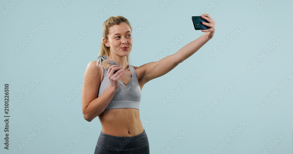 Obraz premium Woman, water bottle and selfie in studio for fitness, influencer and social media for gym space. Person, memory or post with content creation for exercise club, confidence and drink on background