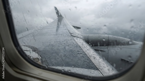 Raindrops on airplane passenger window with view of wing during storm