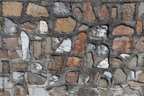 Fotografia Natural stone wall with flat sandstone, porphyry, calcareous rock, and white quartzite assembled in dark cement mortar