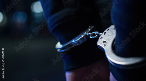 Handcuffs on wrists of person in dark clothing, symbolizing arrest and law enforcement at night