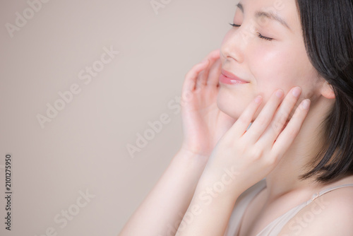 ピンクベージュ背景笑顔の美しい目を閉じる日本人女性の手を触れる横顔　美しい肌とナチュラルメイクの美容クローズアップポートレート