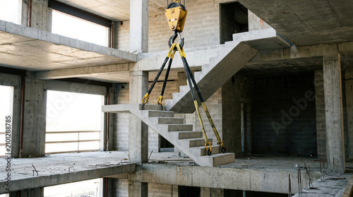 Fotografie Crane hook lifting concrete staircase in unfinished building construction site