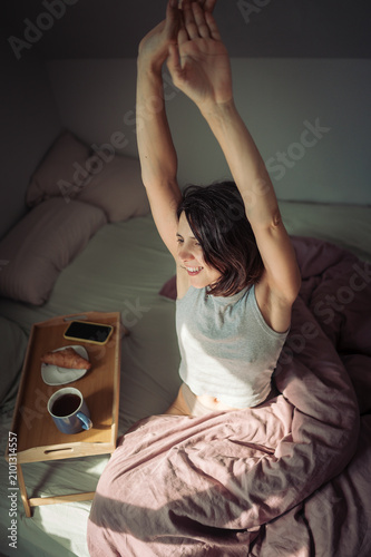 Smiling adult stretching in bed with breakfast tray