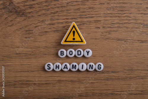 Cuadro en lienzo Body shaming message with letter beads and a caution symbol on a wooden background, representing bullying, discrimination, mental health awareness, self esteem, and respectful communication