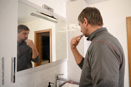 фотографія Middle-Aged Man Brushing His Teeth in Bathroom Mirror, Morning Hygiene Routine