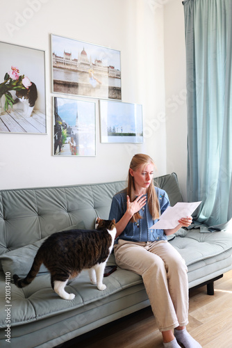 Woman reviewing a letter with concern while her cat keeps her company, home life and everyday emotions.