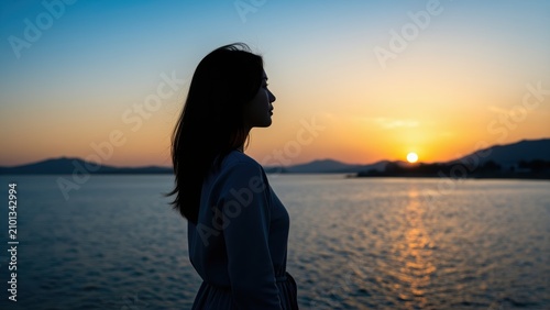 Solitude by the Sea: A young woman stands silhouetted against a breathtaking sunset over the calm ocean, her profile a picture of quiet contemplation and serene beauty.