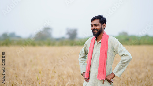 young indian farmer standing at golden wheat field