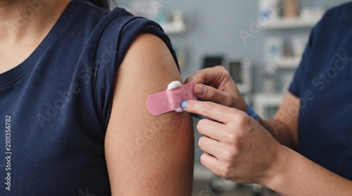 Nurse applying a medical adhesive bandage on the arm of a patient after a routine vaccination or injection procedure at a clinic