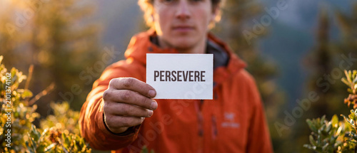 Young man holding a sign that says persevere outdoors in nature
