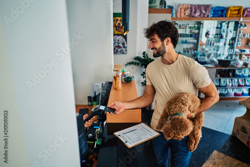 Man paying with smartphone in pet shop holding dog