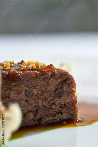 Macro shot of roasted meat glazed with mustard seeds, served with cauliflower and gravy on a white plate. Elegant fine dining close-up.