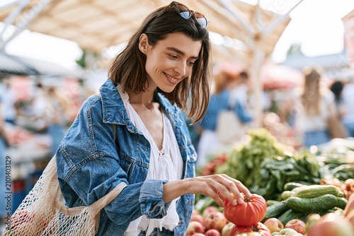 Young woman shopping for fresh produce at an open-air market while enjoying a sunny day