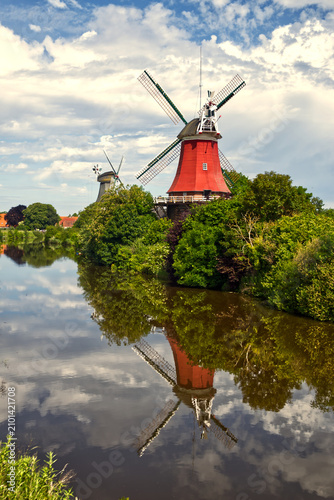 Fotografie Windmills of greetsiel, germany, reflecting in tranquil canal water