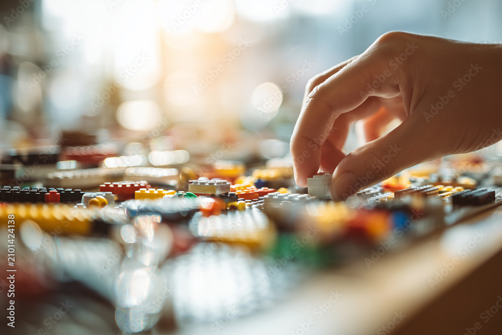 Fototapeta premium Fingers assembling colorful LEGO bricks on a smooth indoor surface during a creative building session