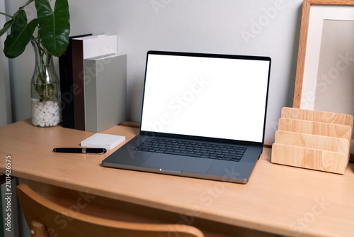Laptop with blank white mockup screen on wooden desk in minimalist office.